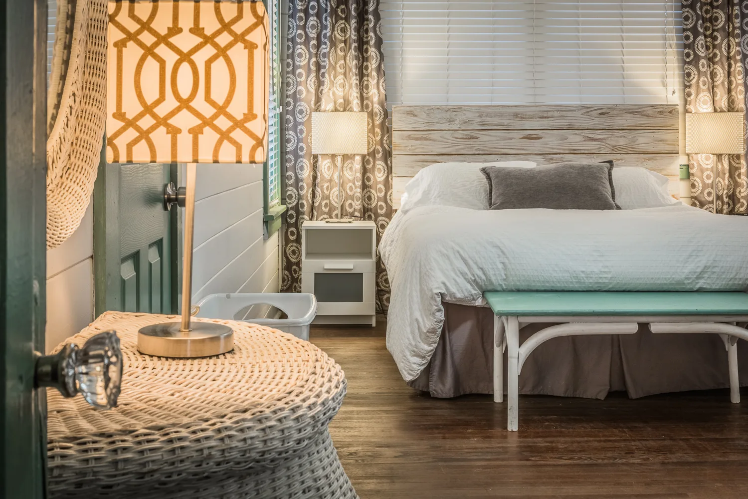 Cozy bedroom with whitewashed headboard, patterned lamp, and aqua bench
