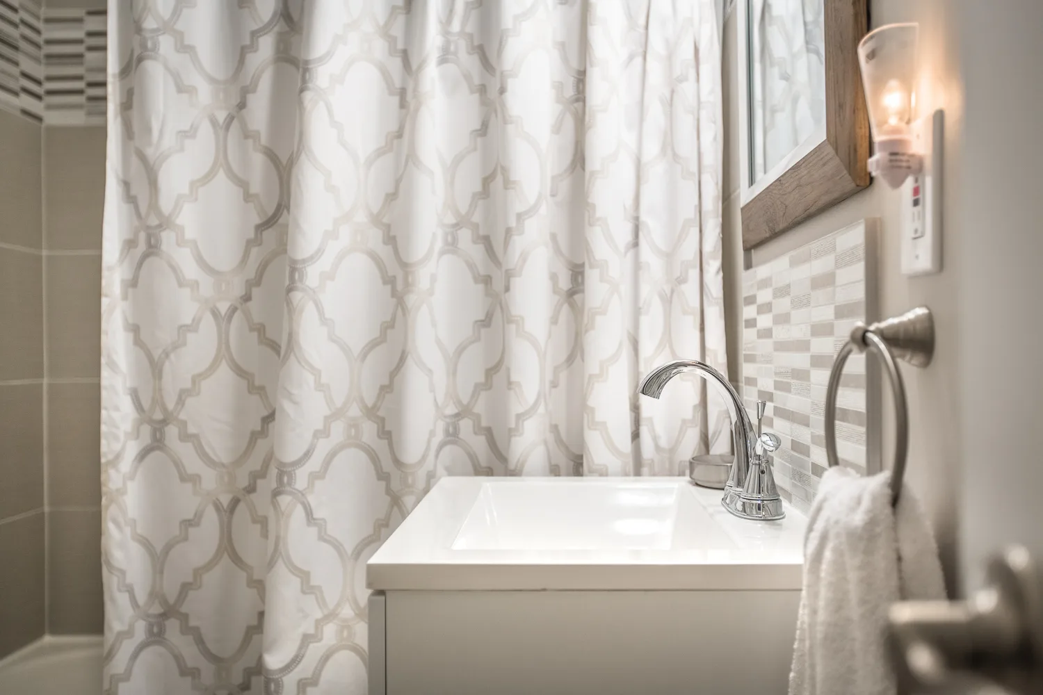 White bathroom vanity with chrome faucet and patterned shower curtain