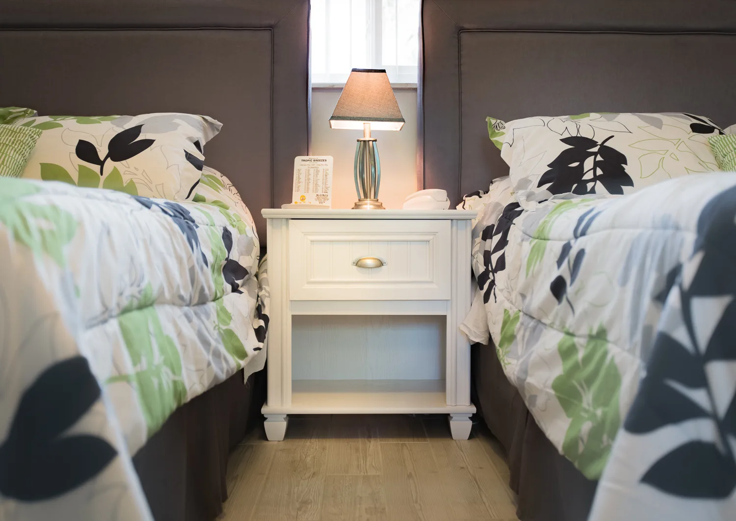 Two beds with botanical print comforters flanking a white nightstand