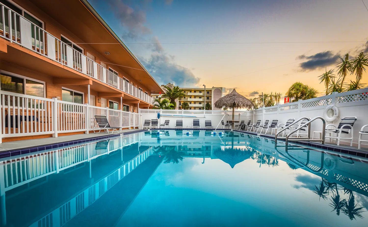 Sparkling pool with lounge chairs and tiki umbrella at sunset
