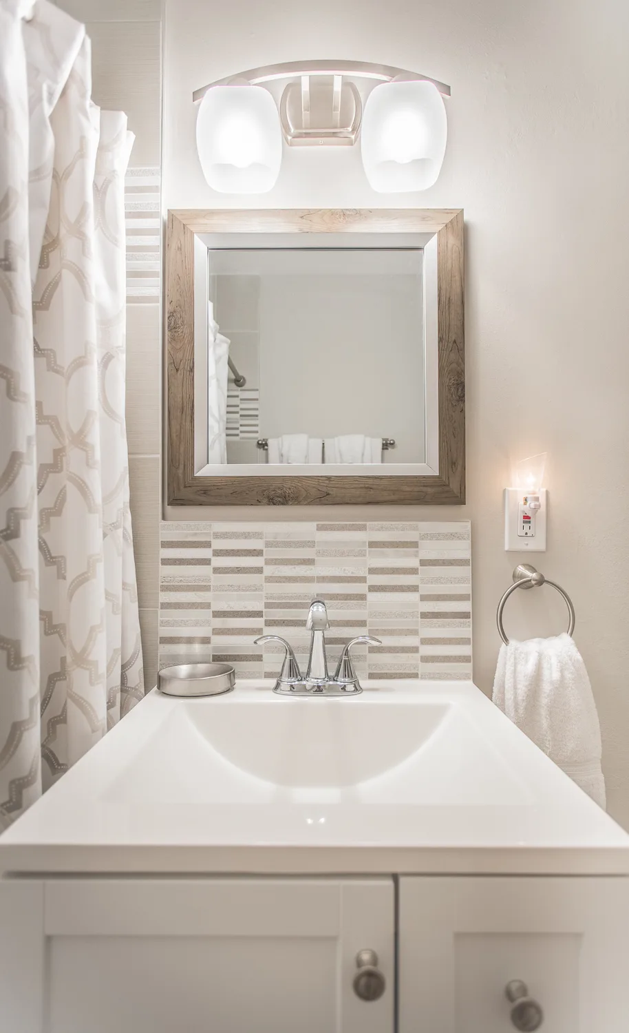 Compact bathroom vanity with wood-framed mirror and neutral mosaic tile