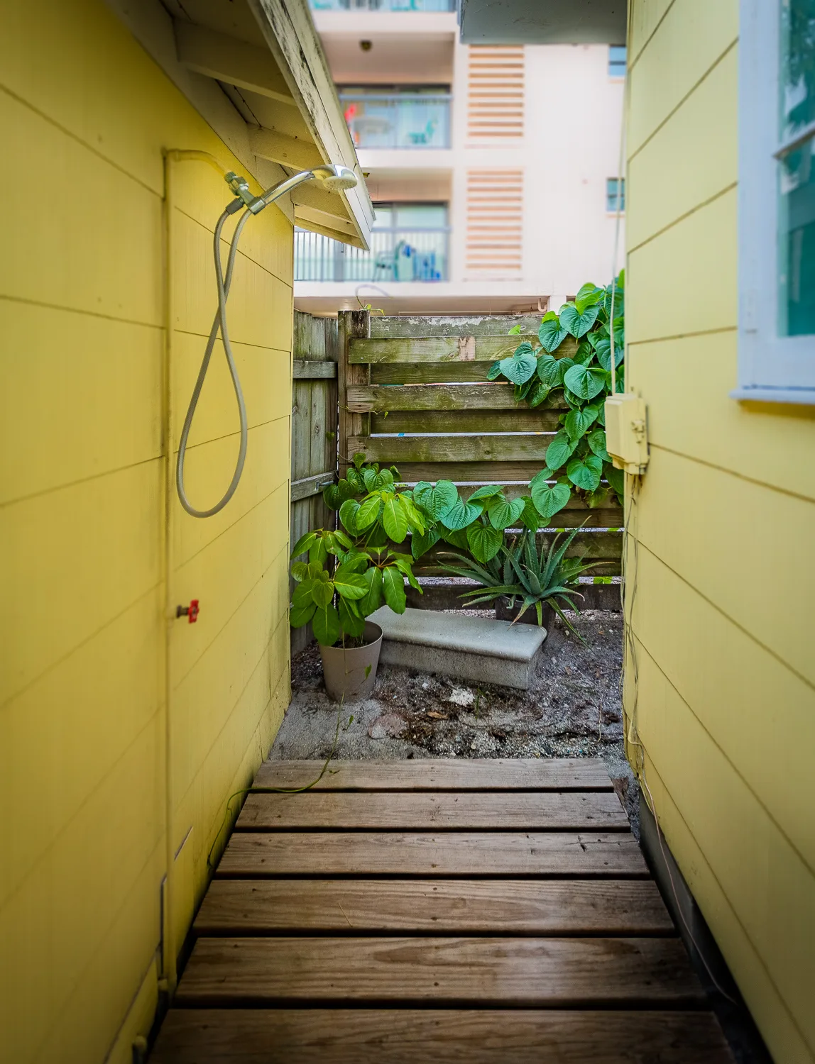 Private outdoor shower on a wooden walkway between yellow cottage walls