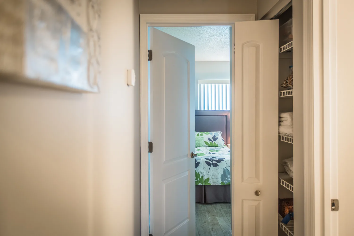 Hallway with linen closet shelves opening to a bright bedroom