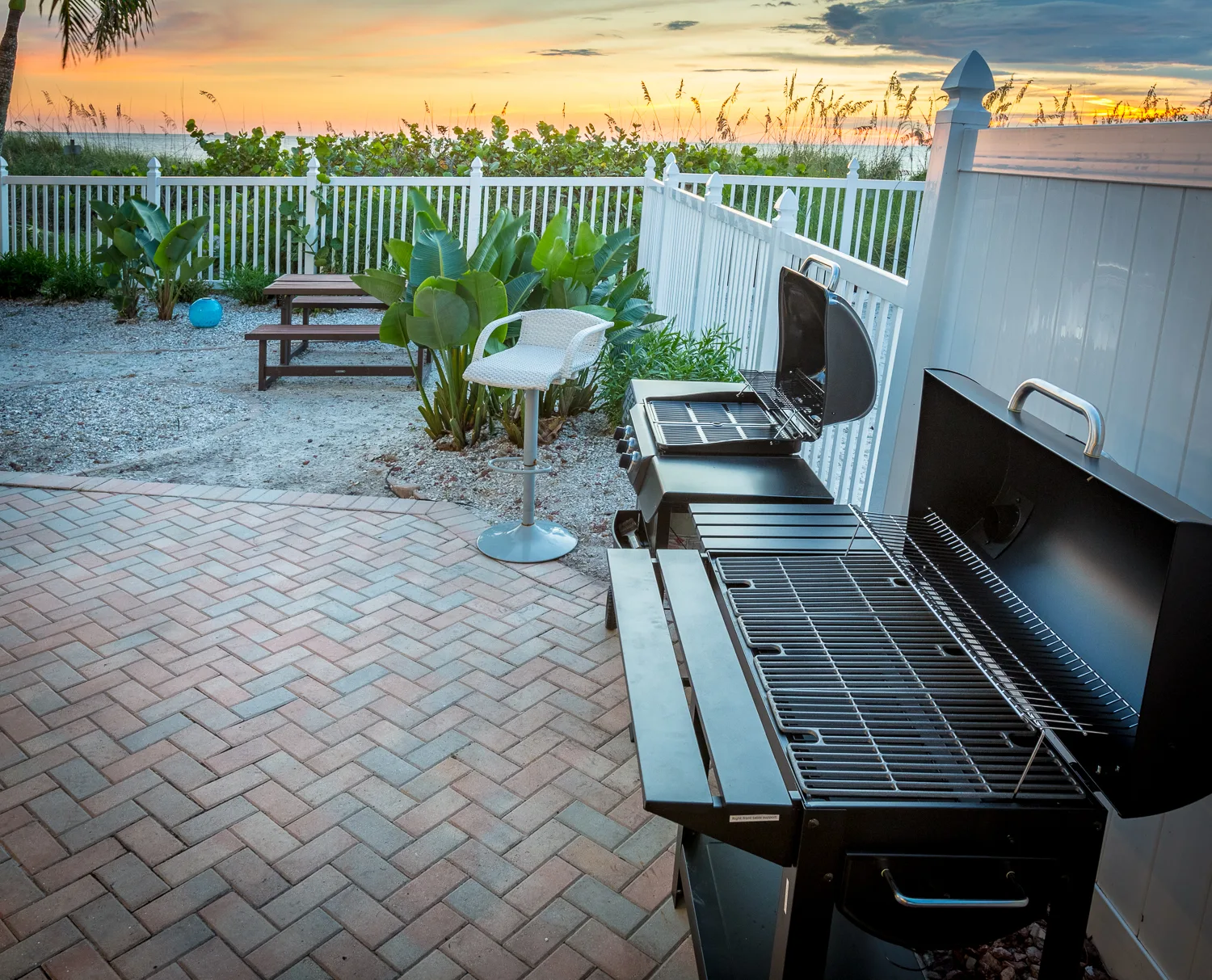 Gas grills on a brick patio beside dunes at sunset