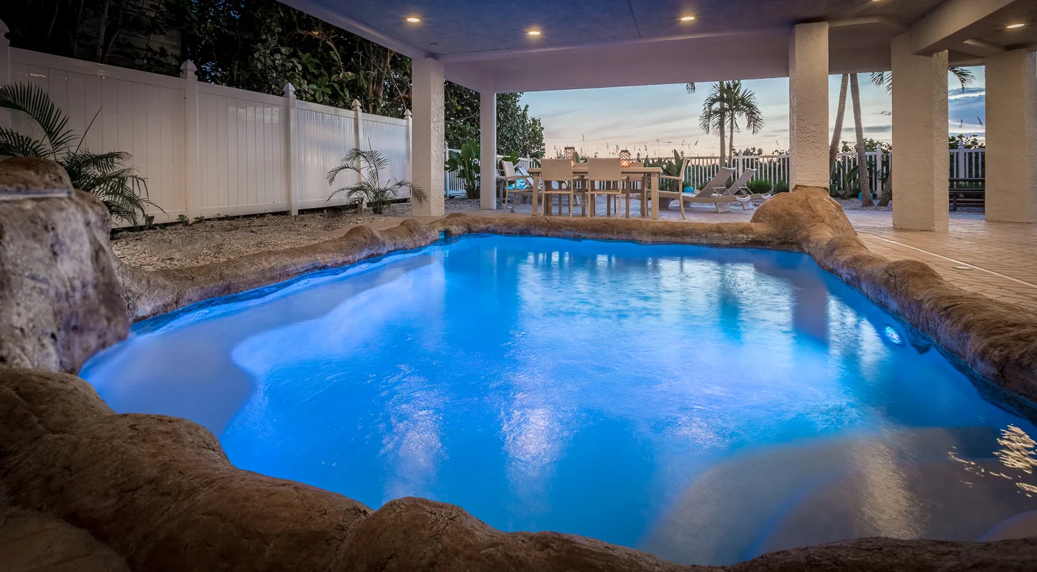Lagoon-style pool glowing blue beneath a covered patio at dusk