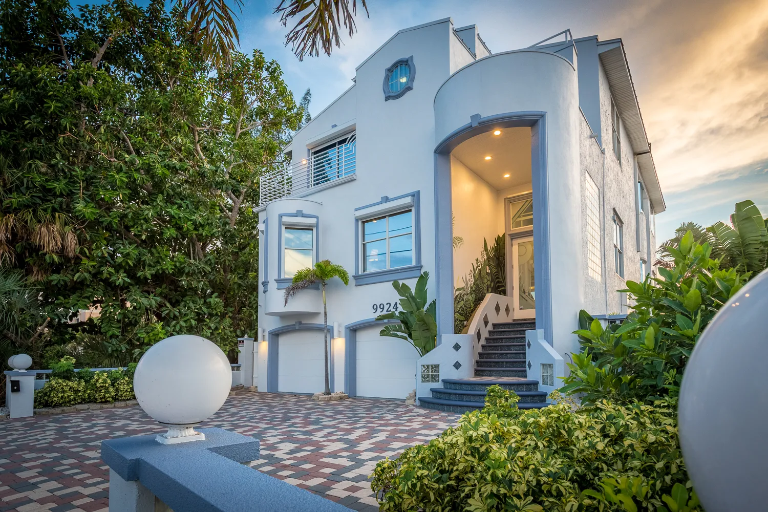 Multi-story coastal home exterior with landscaped drive at dusk