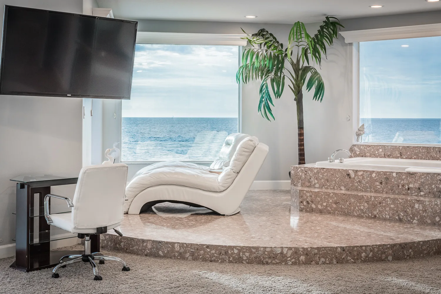 White chaise lounge and soaking tub beside ocean-view windows