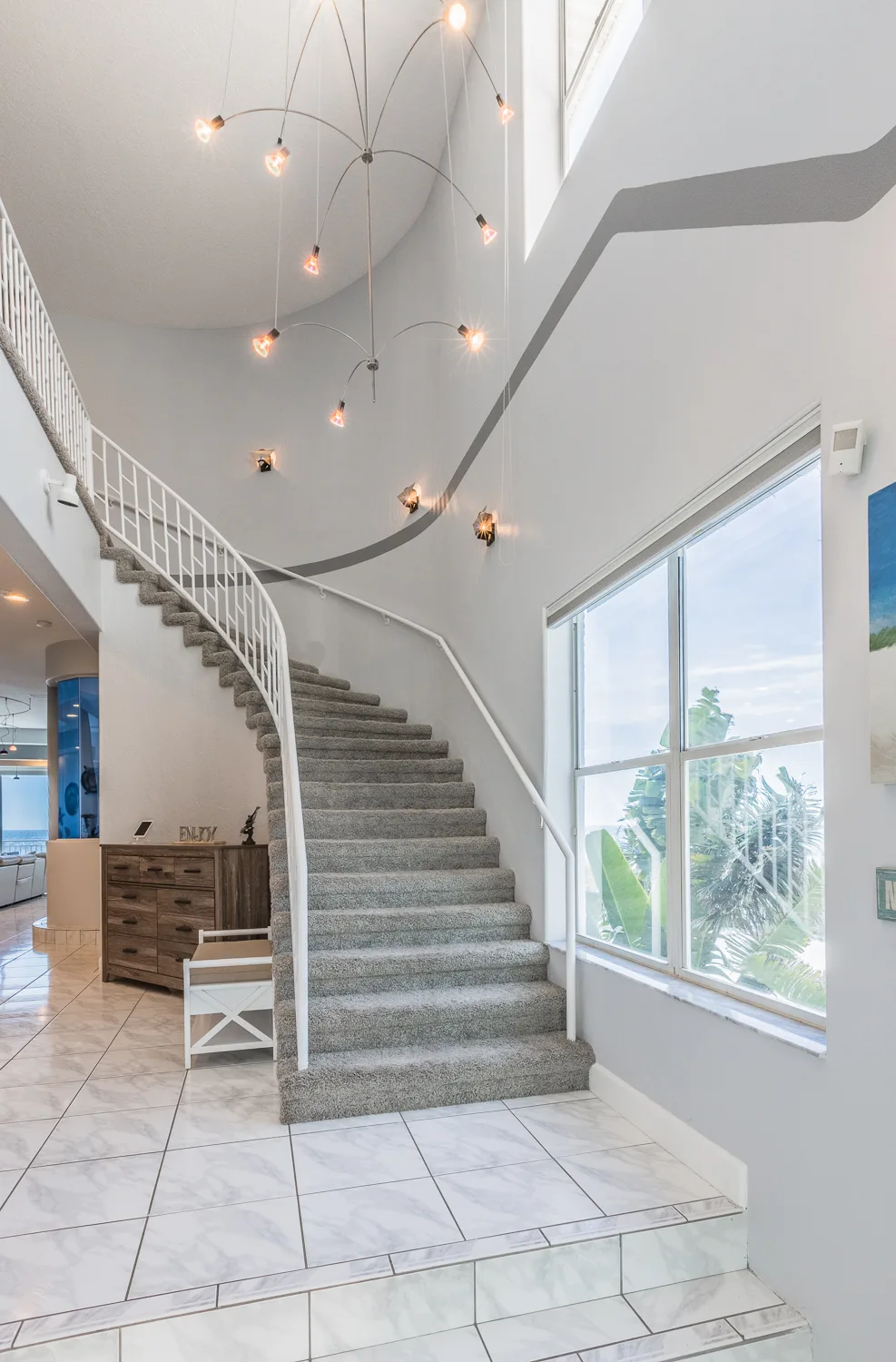 Curved carpeted staircase beneath cascading pendant lights and a bright window