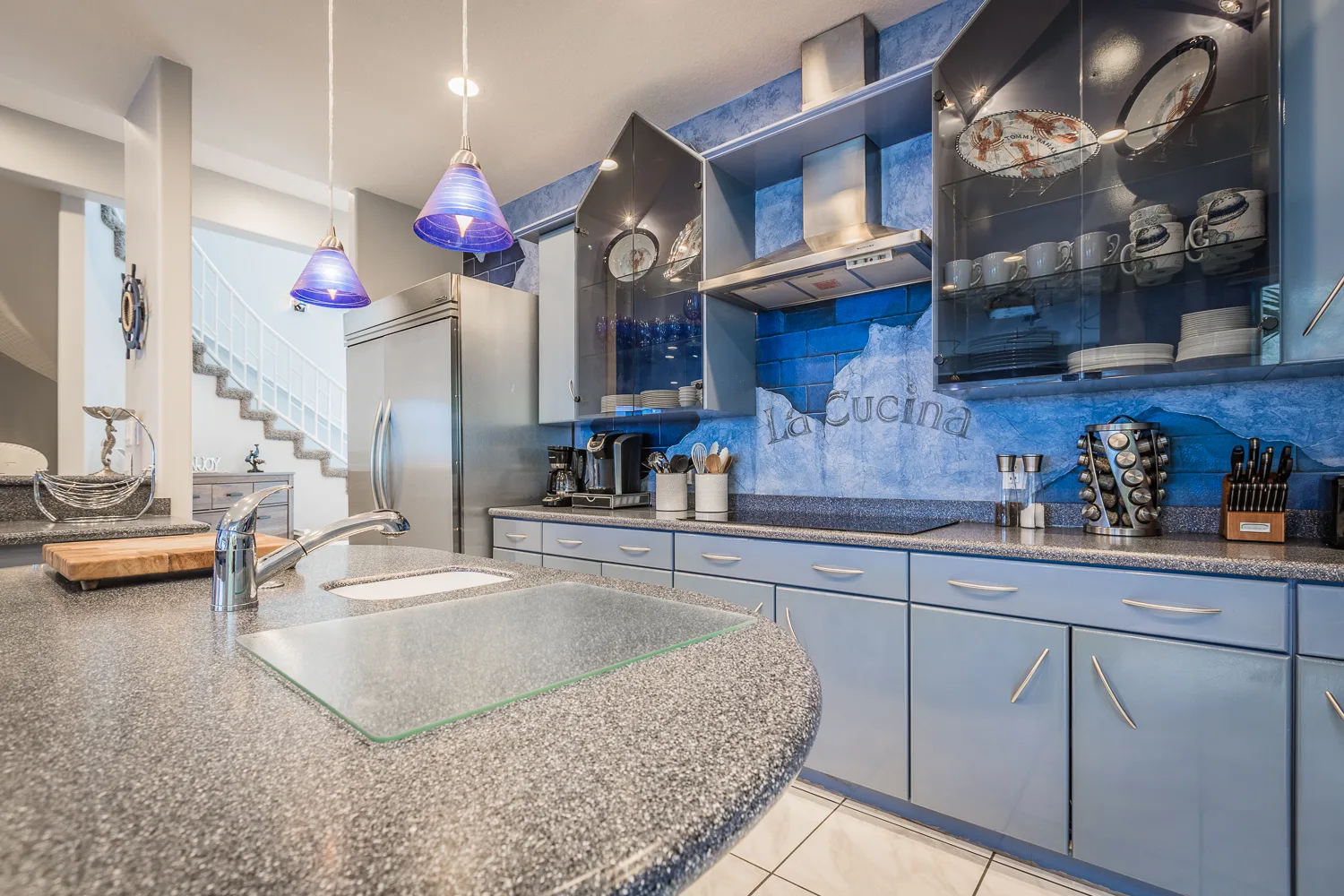 Kitchen with blue cabinetry, speckled granite island, and glass pendant lamps