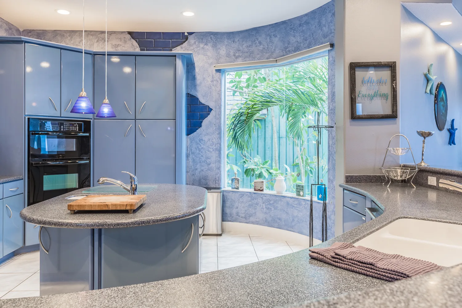 Blue kitchen with curved island and bay window framing palms