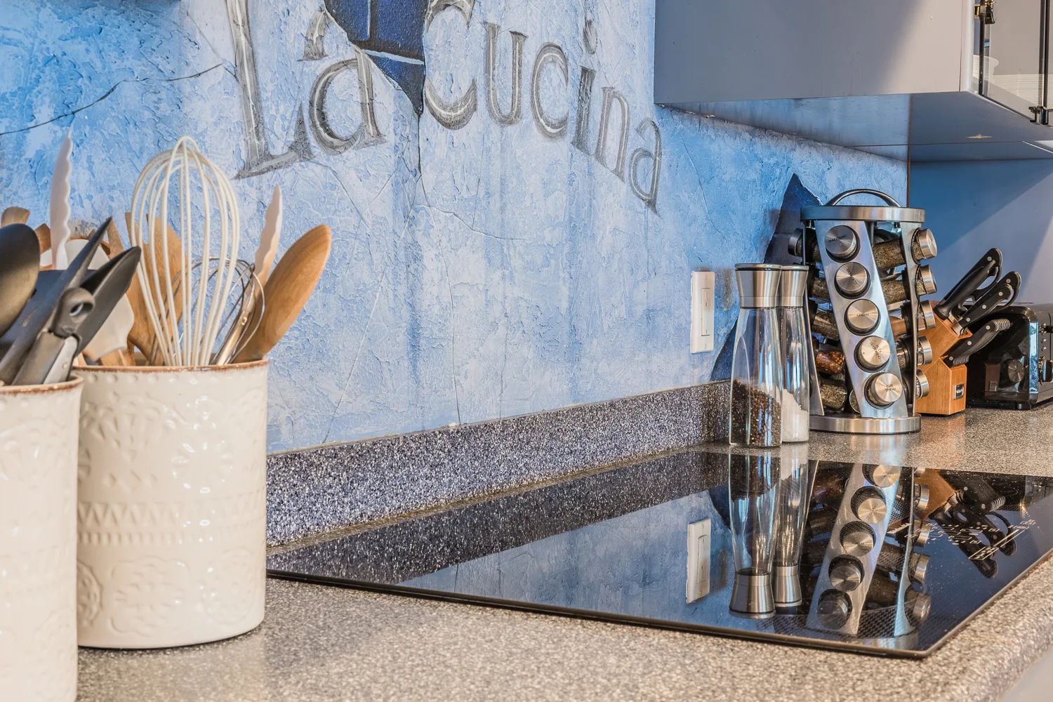 Kitchen cooktop with utensil crocks and spice rack against painted backsplash