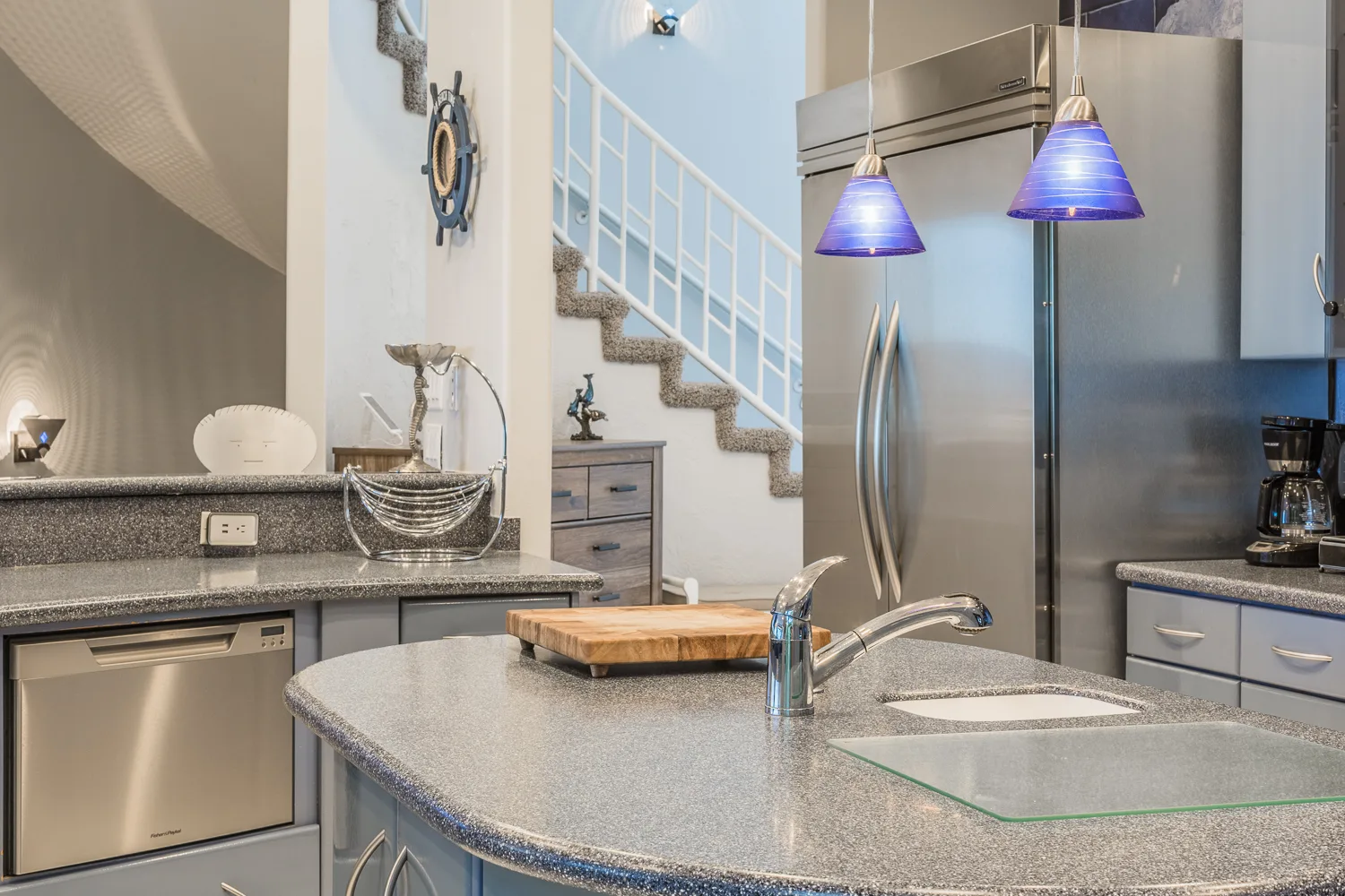 Kitchen island with cutting board, stainless refrigerator, and staircase beyond